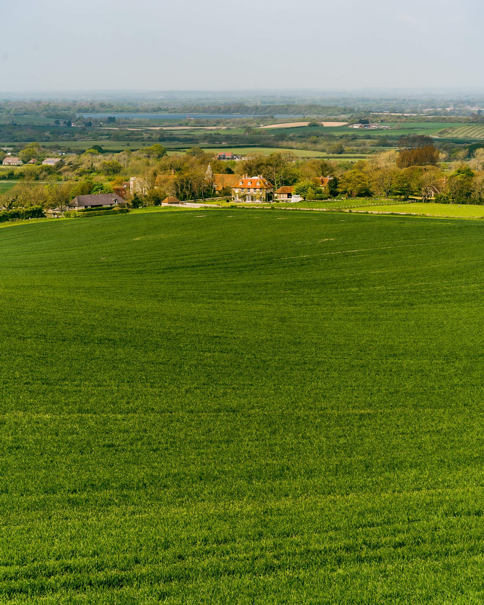 Farmlands stretching towards buildings of Wilmington village, East Sussex, England, UK